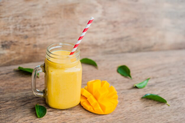 Mango smoothie in a glass jar with a striped red straw