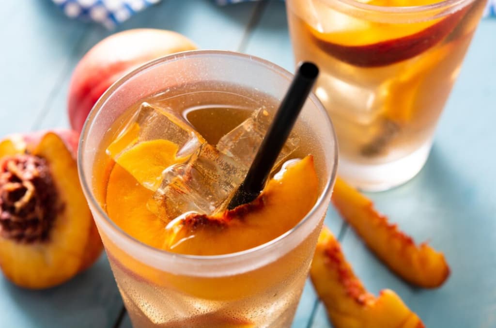 Peach slices in a glass of iced tea with a straw, another glass in the background