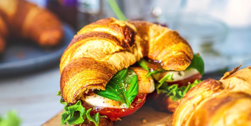 A croissant sandwich filled with fresh greens, tomatoes, and cheese on a wooden board