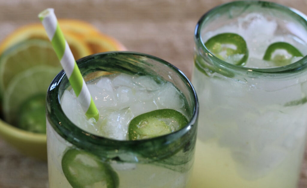 Two glasses of classic lime margaritas with ice, garnished with lime slices, served with a striped straw