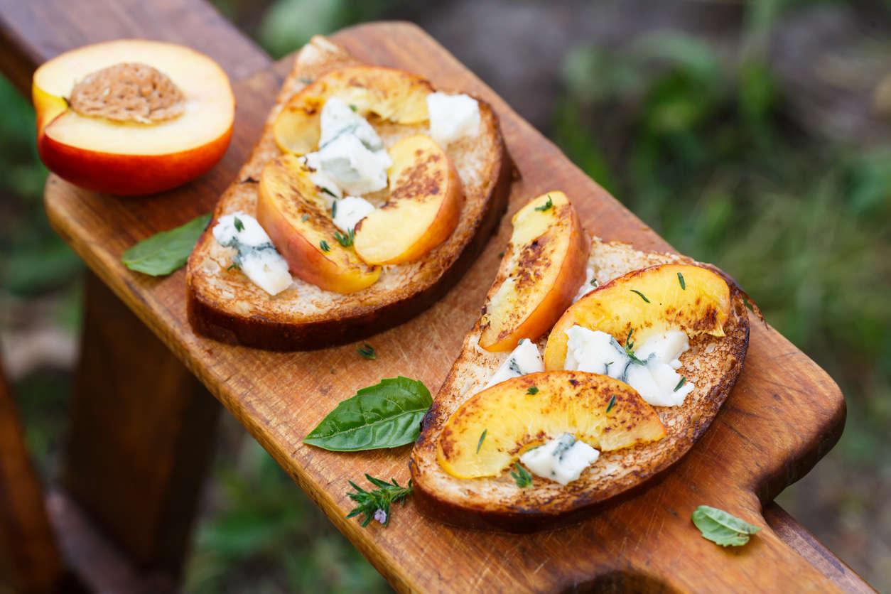 slices of toasted bread with roasted peach slices, blue cheese, and mint stems on a wooden board
