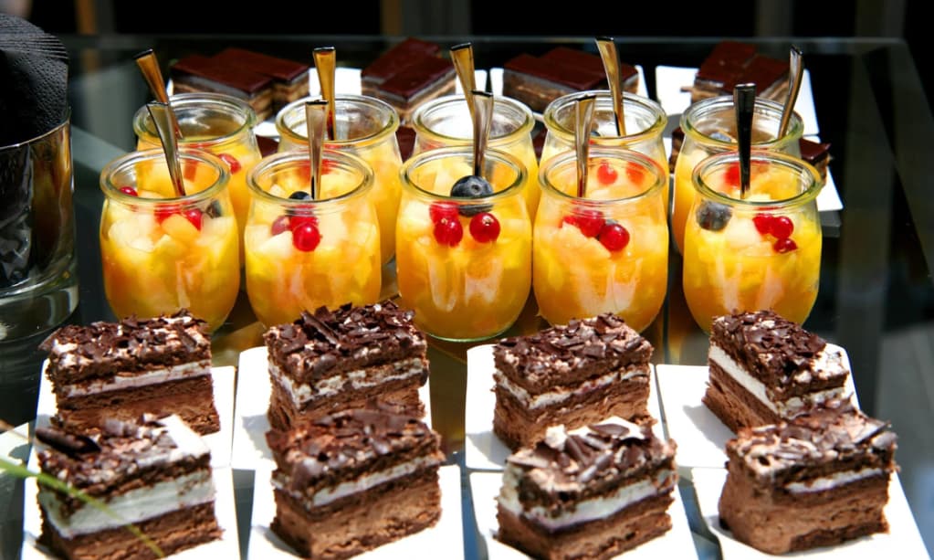 A selection of desserts with fruit cups and layered chocolate cakes on a serving table