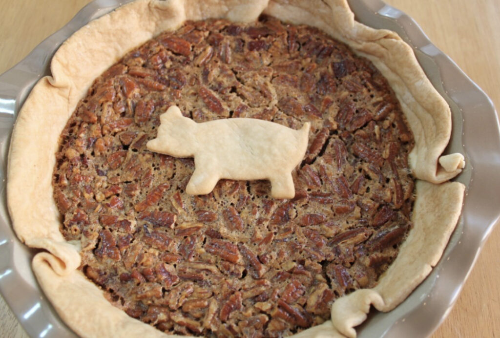 A freshly baked pecan pie with a pastry pig decoration on top