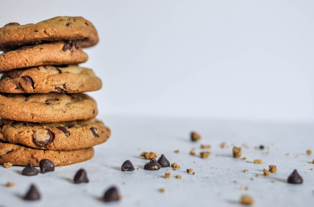 Chocolate chip cookies stacked with crumbs and chocolate chips on a light surface